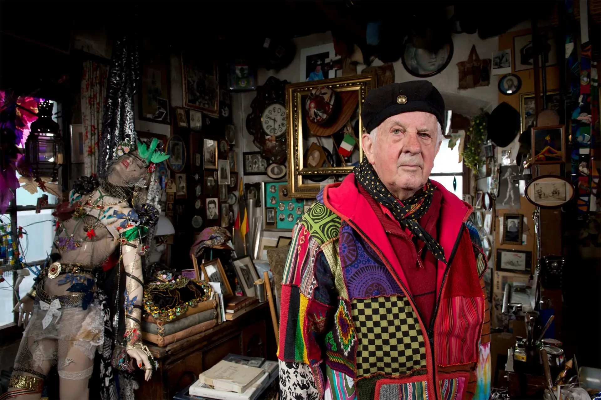 Bernard Viglino debout dans son cabinet de curiosités, entouré d'objets, tableaux et mannequins décorés